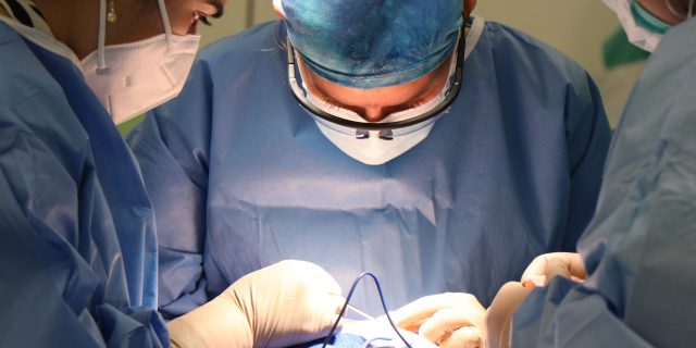 Surgeons in operation room wearing masks and gloves performing surgery.